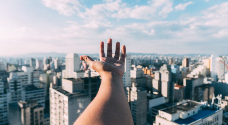 ciudades sostenibles, imagen de una mano por encima de una ciudad con cielo despejado